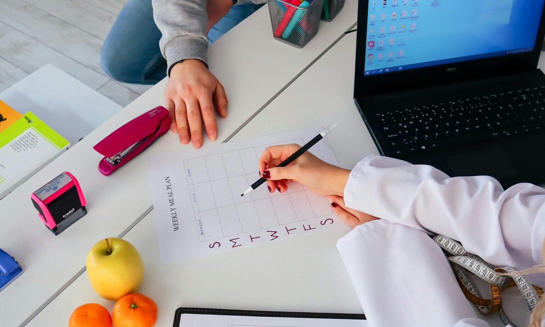 A nutritionist and a patient discuss a weekly meal plan in a modern office setting.