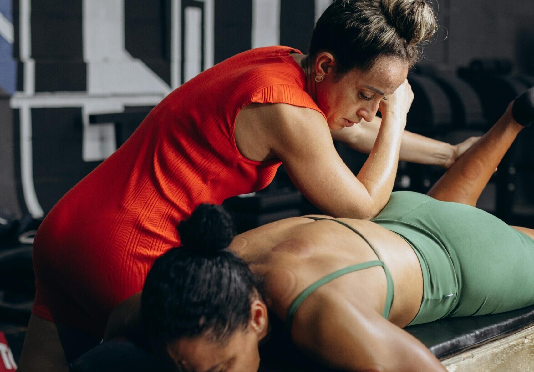 A therapist performs deep tissue massage on a client in a gym environment.